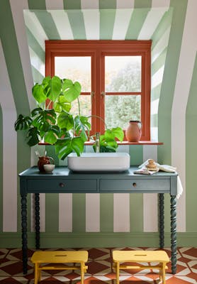 Bathroom featuring light green and white striped wallpaper (Broad Street - Pea Green) with a basin underneath a window.