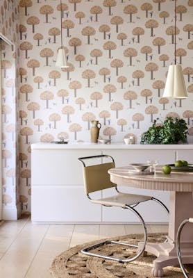 Dining room featuring pale pink tree print wallpaper (Rodney Street - Masquerade) with a white cabinet, dining room table and chairs.