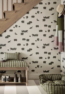 Hallway space featuring neutral dog and sheep print wallpaper (Nip & Lassie - Slaked Lime - Dark) with a dog sat in a bed on the right and stairs to the left.