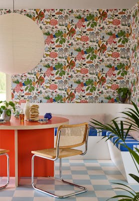 Breakfast room featuring multi-coloured wildlife print wallpaper (Animal Kingdom - Atomic Red) with a bright red table and wicker chairs next to a banquette.