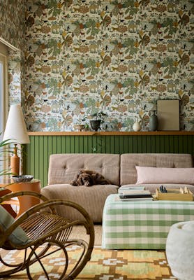 Living space featuring green wildlife print wallpaper (Animal Kingdom - Pea) with green panelling behind a sofa, foot stool and a rocking chair.