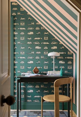 Home office space featuring car print wallpaper (Road Trip - Pleat) on the back wall and striped wallpaper on the right (Broad Stripe - Pleat) with a desk and chair.