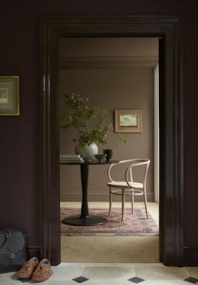 Hallway painted in aubergine shade 'Cordoba' looking into a study painted in mid-brown shade 'Scullery' with a chair and table.